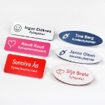 Navneskilt for sykepleier med nål eller magnet. Gravert navneskilt med navn og motiv,  hjerte, sprøyte, smiley osv. Ovale eller rektangulære skilt i farger, rosa, hvitt, blått, rødt og flere farger tilgjengelig.